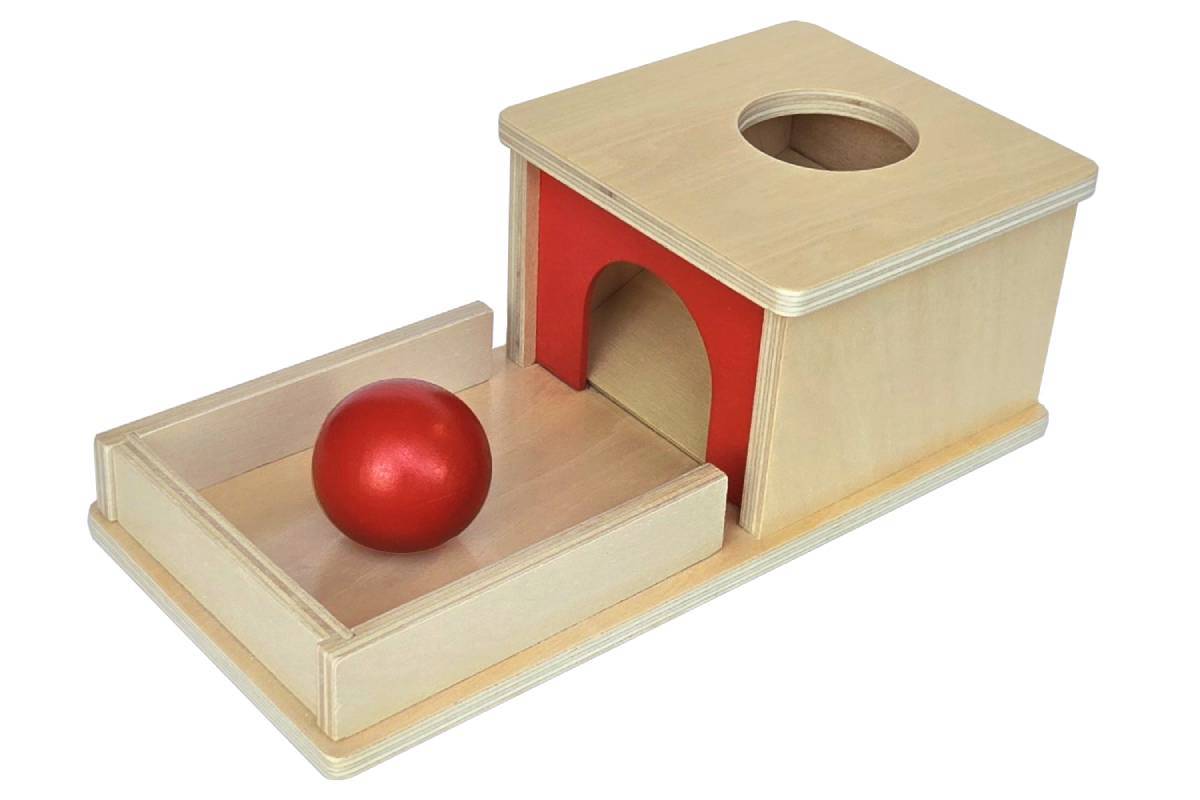 Object permanence box with tray. Natural wood with red accent and red wooden ball. Box has a circular hole for the ball to be dropped into, and a ramp for the ball to roll back out on.