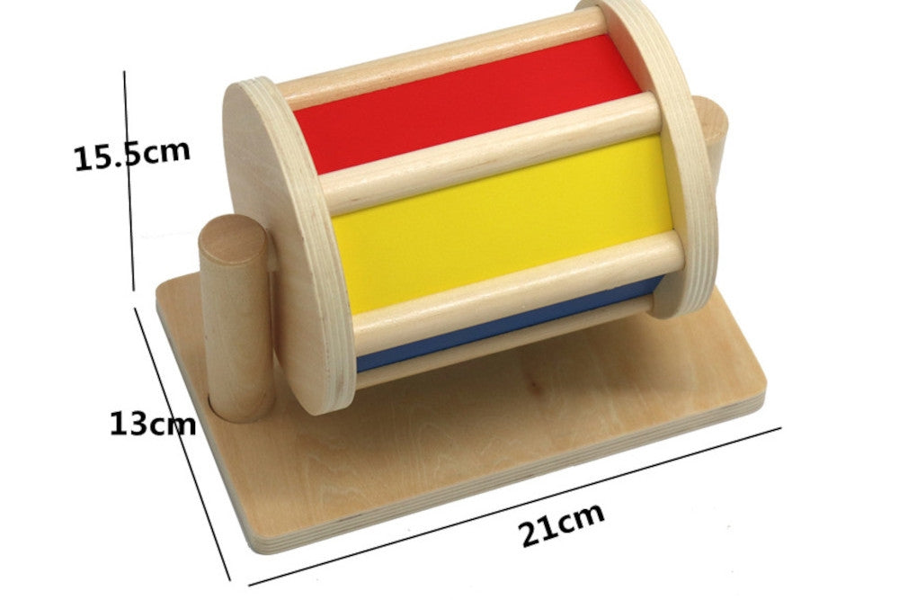 Colourful wooden spinning drum measuring 15.5. cm x 13 cm x 21 cm. Three sides in red, yellow, and blue are visible.