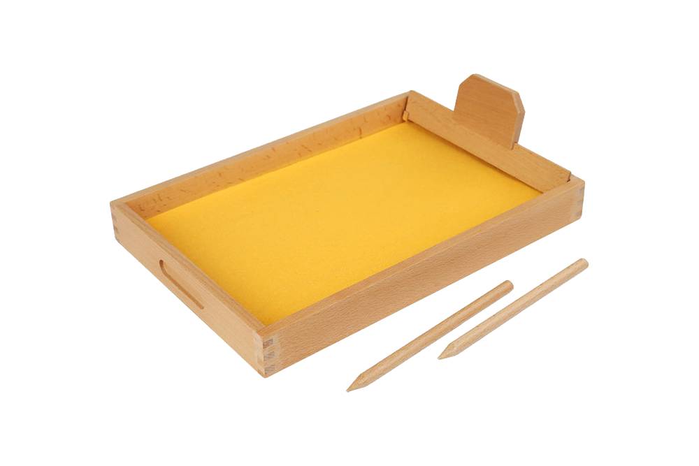 Wooden tracing tray filled with yellow sand. A smoothing tool rests on the side of the tray, recently used. Two wooden "pens" lie beside the tray.