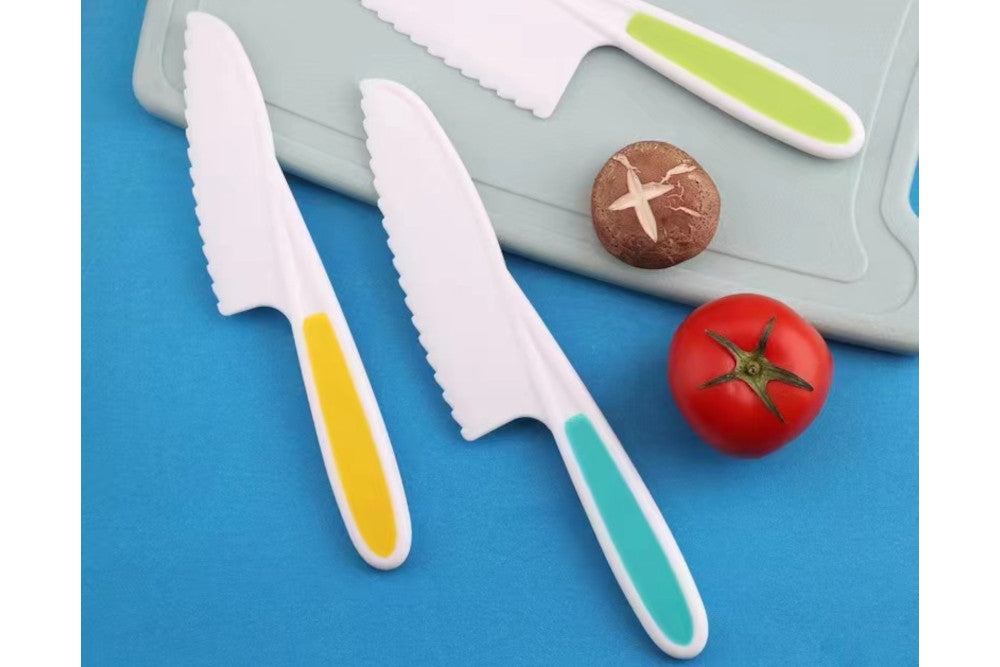 Three white serrated plastic knives on a cutting board with a mushroom and a tomato.